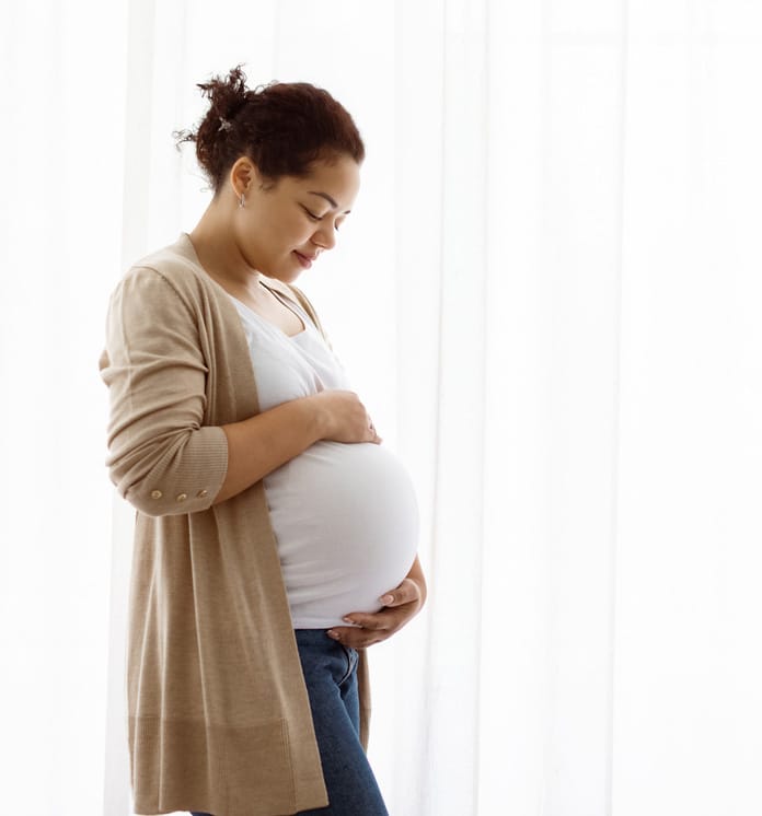 Pregnant woman standing by a window thinking about adoption for her baby